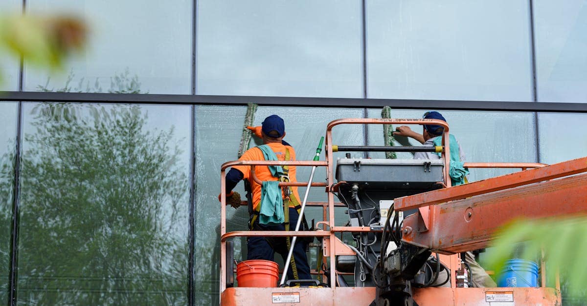 Two workers cleaning windows on a glass building facade using a lift platform, enhancing building aesthetics.